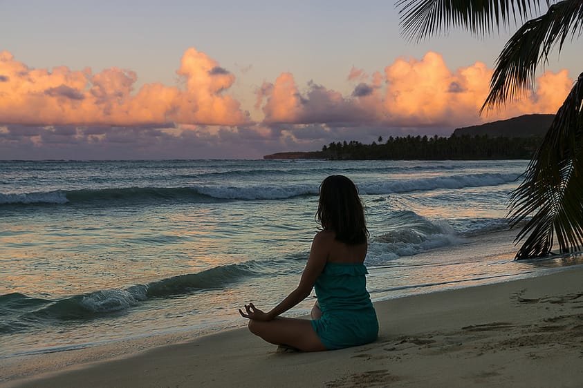 A woman meditates and practices yoga on the beach as part of her outdoor therapy.