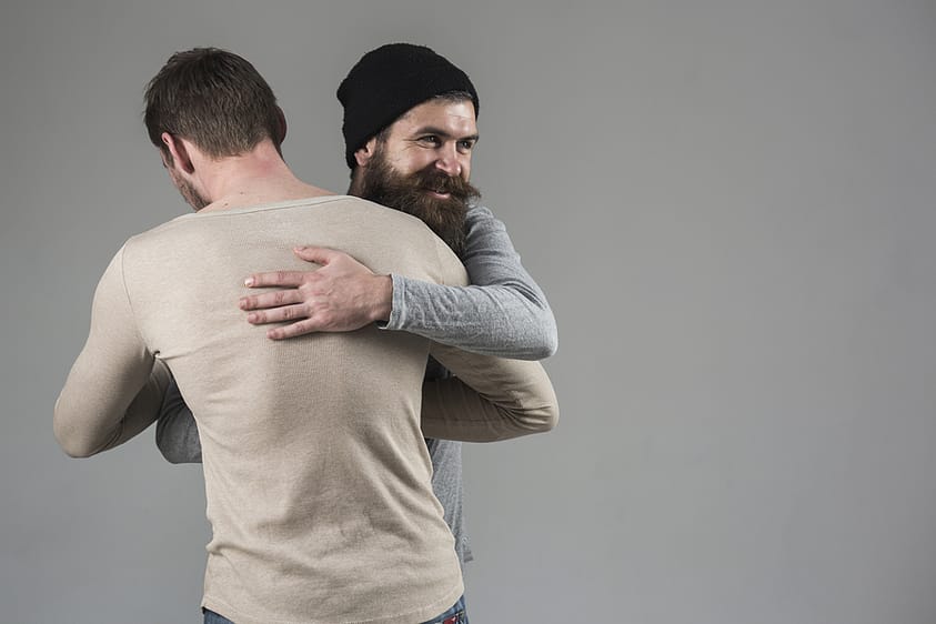 Two men hug in therapy unencumbered by the pressures of masculinity.