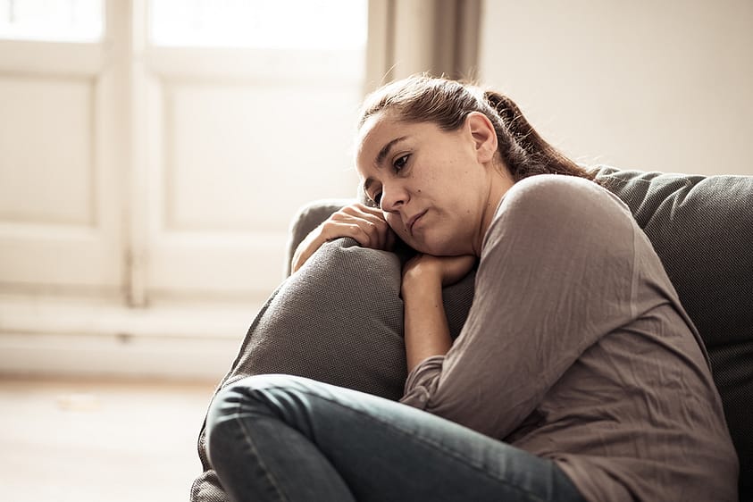 A young woman curls up on the couch feeling hopeless and sad, early signs of depression.