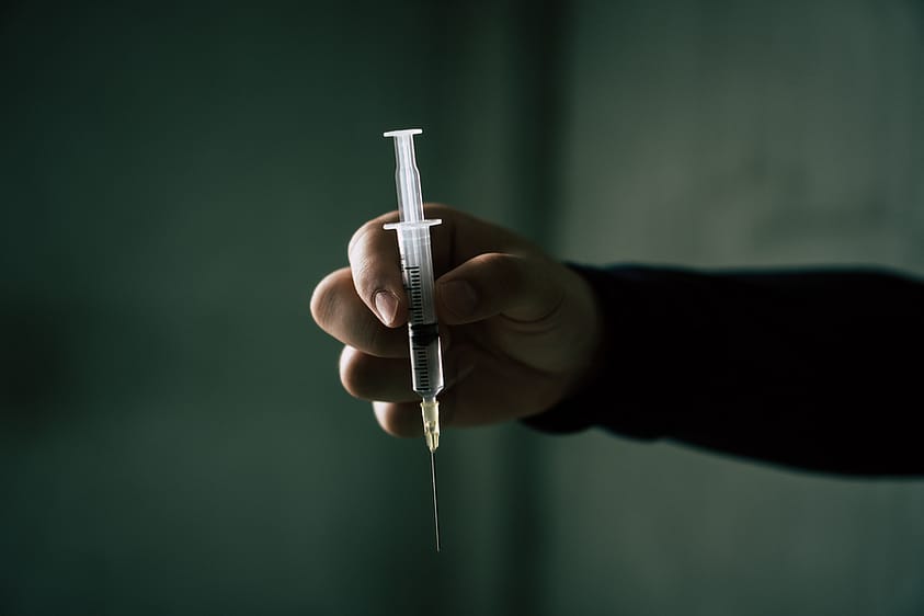 A hand holds a syringe in front of a dark background.