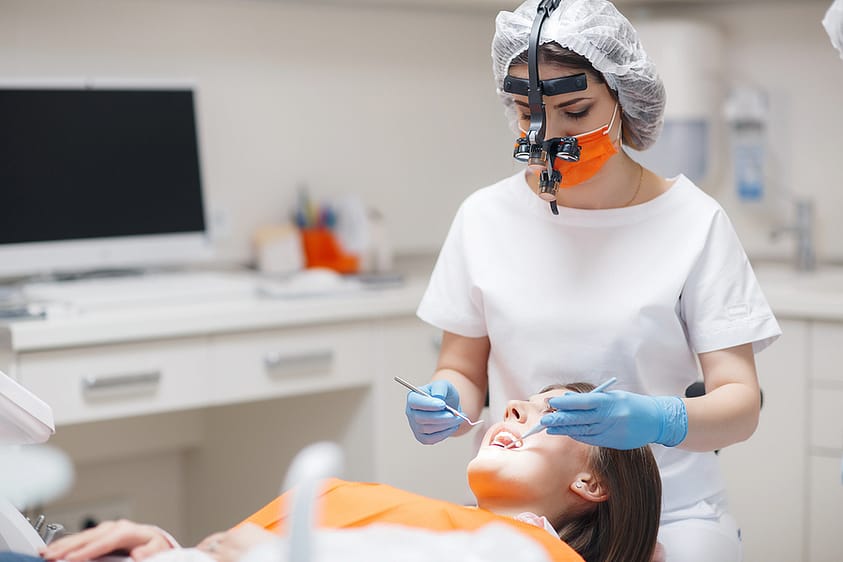 A woman getting her teeth checked and cleaned by a dental assistant.