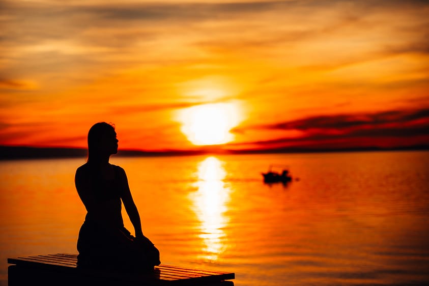 A woman meditating during sunset on the ocean.