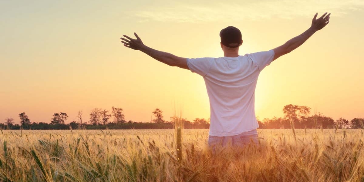 a man stretches out his arms towards the sunrise as he experiences sober living
