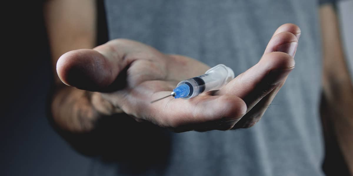 Hand holding syringe demonstrating signs of heroine addiction