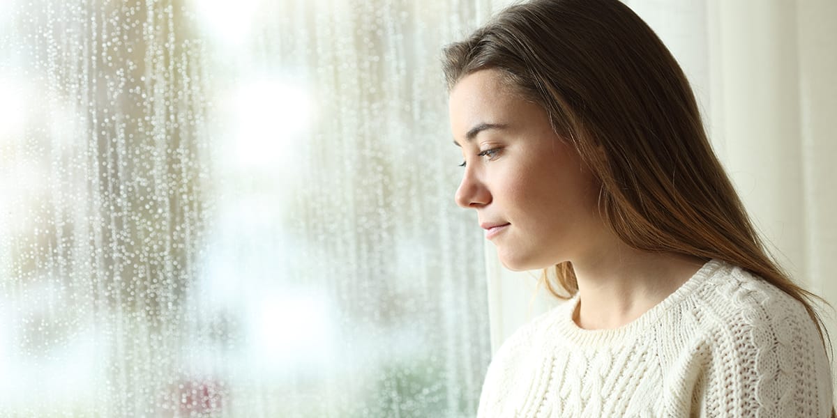 a woman looking out a rainy window thinking about signs of stress