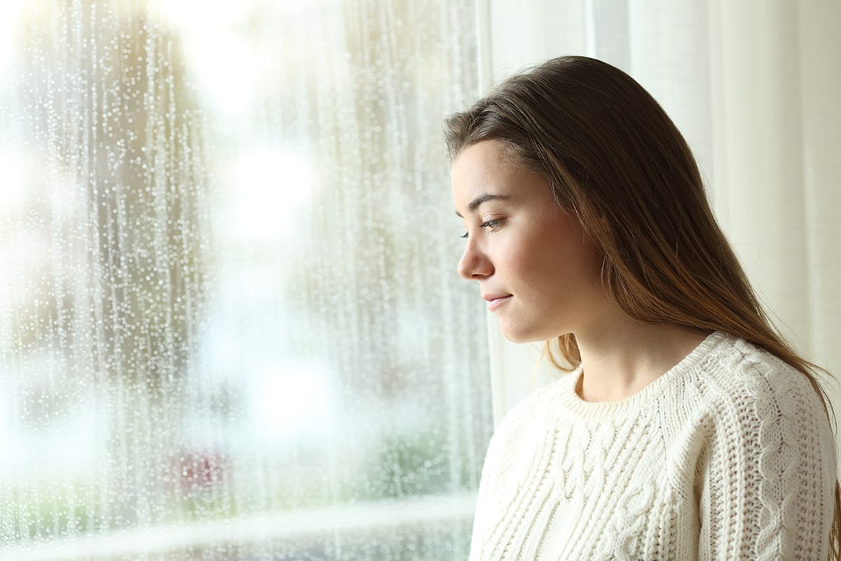 a woman looking out a rainy window thinking about signs of stress