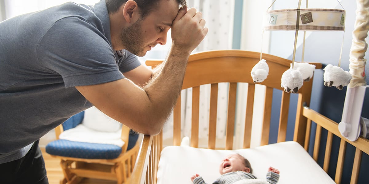 man leaning against his baby's crib suffering from symptoms of postpartum depression for men