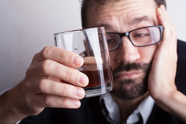 a man drinking and suffering from Stages of Alcoholism