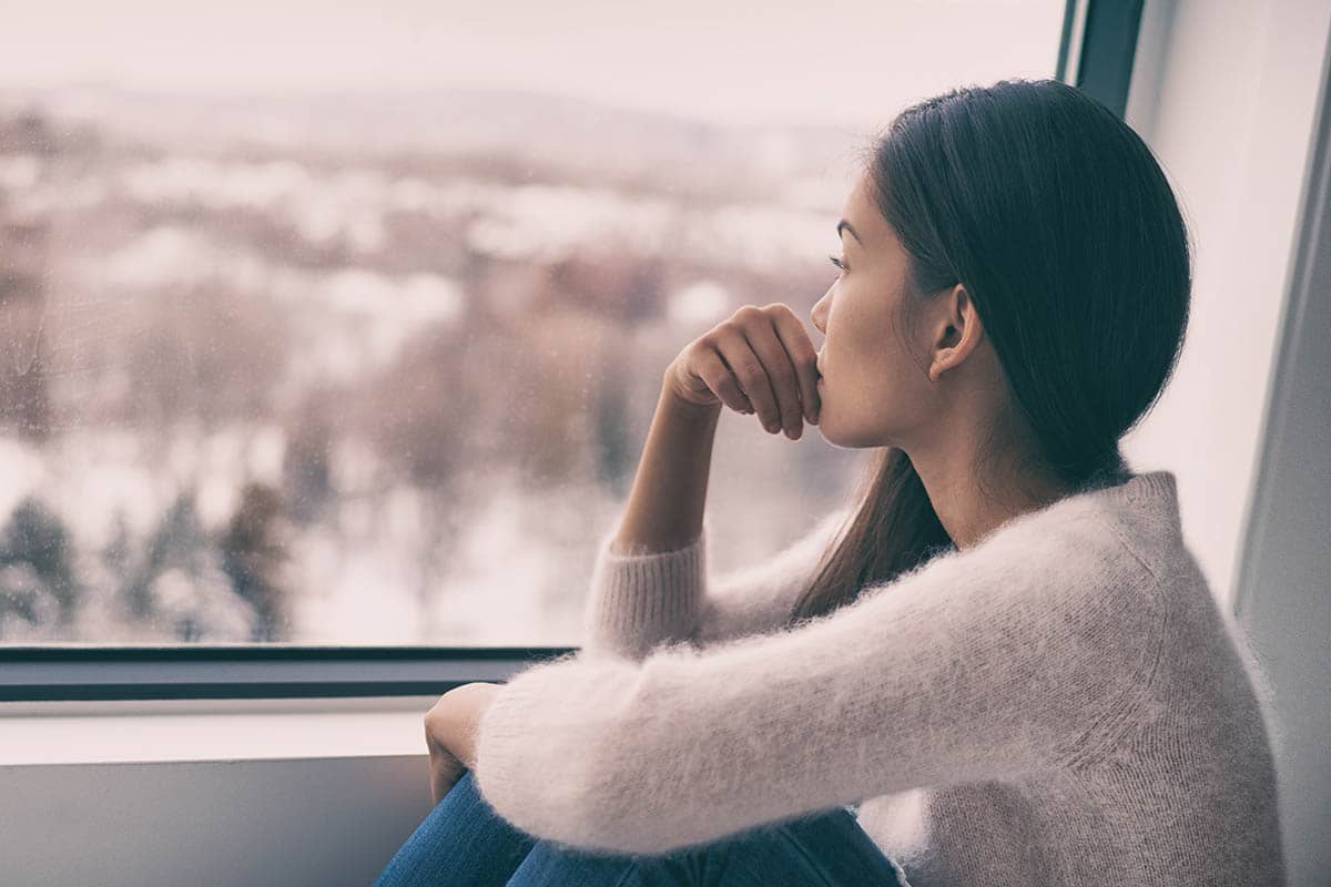 a woman looking out a window struggling from signs of depression