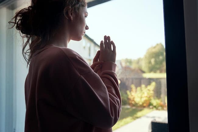 a woman looking out a window thinking about postpartum depression in new mothers
