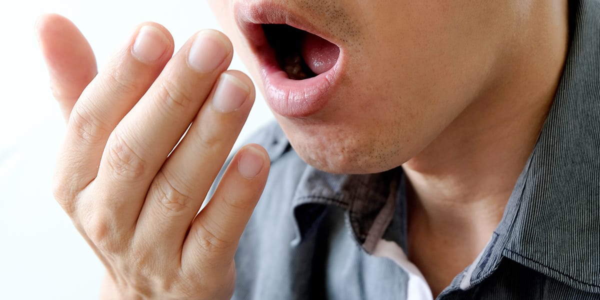 man blowing into his hand showing that Alcohol Brings Bad Breath