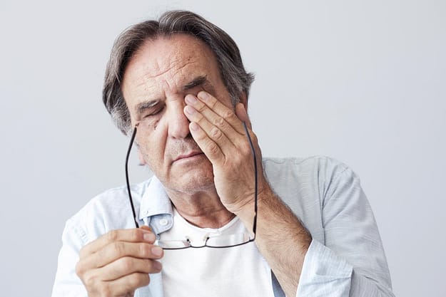 a man rubbing his eyes suffering from long-term effects of alcohol