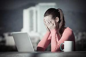 Woman covers eyes as she tries to research anxiety treatment programs on her laptop