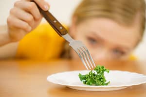 Woman stabs food on plate with fork as she considers anorexia treatment