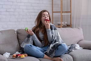 Woman sits on couch and eats as she considers bulimia treatment