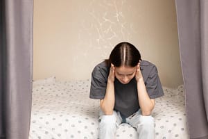 Girl sits on her bed in agony as she wonders what the signs of meth addiction are