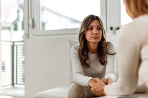 Woman sits on couch and listens to peer talk about her experience in long-term rehab