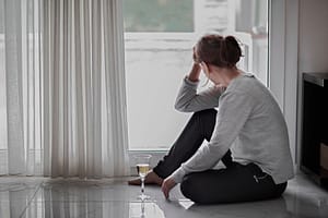 Woman sits on floor with glass of wine as she struggles with alcohol addiction