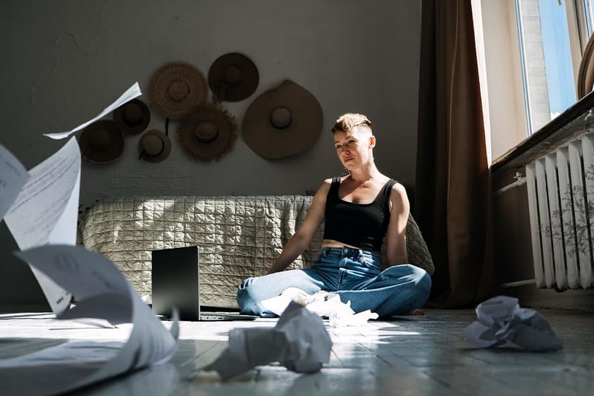 Woman sits on floor with crumbled up pieces of paper after writing, one of the anger management activities she just learned