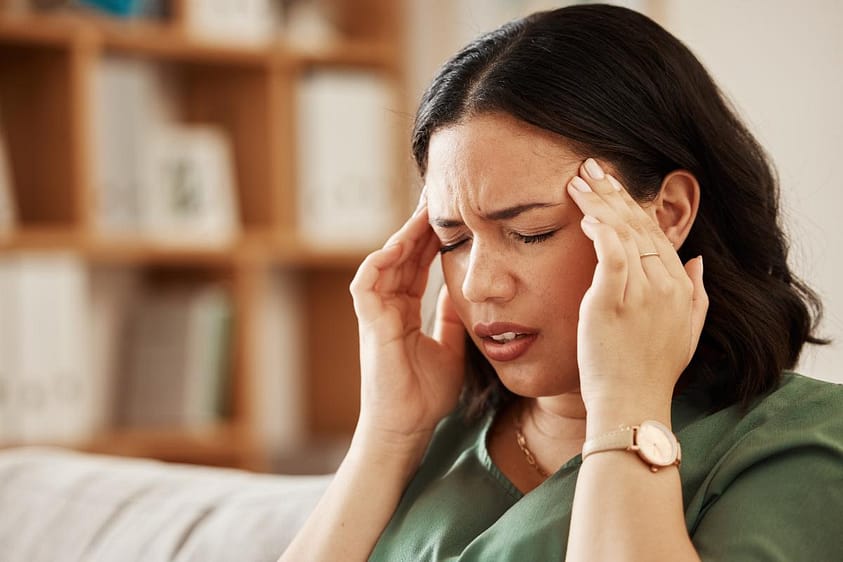 Woman sits on couch nursing headache, pondering how long does fentanyl withdrawal last