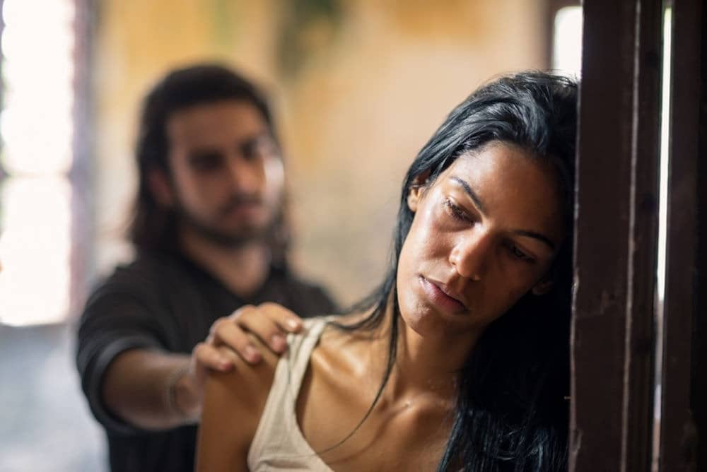 sad woman leaning in doorframe while partner puts hand on her shoulder