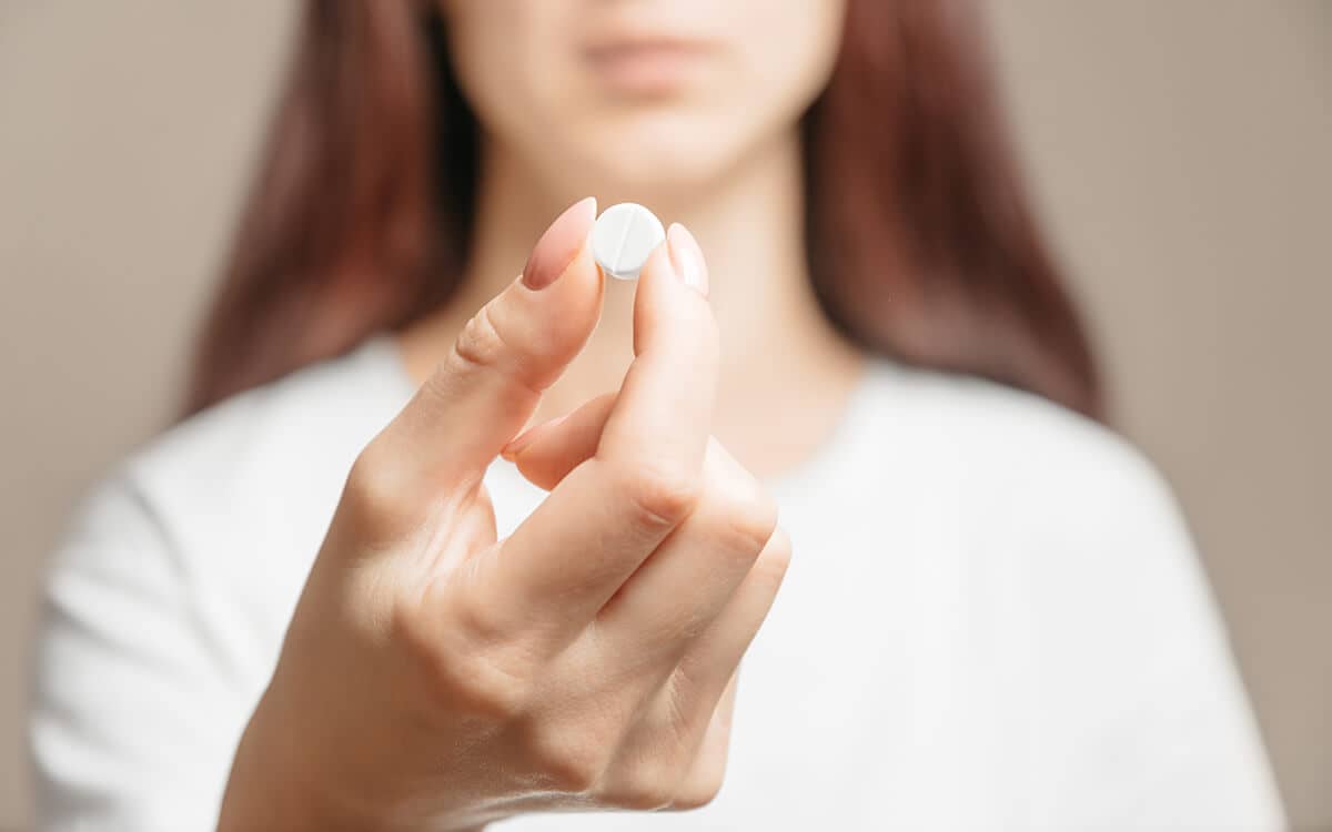 a woman holds a white pill and wonders about the opiate definition