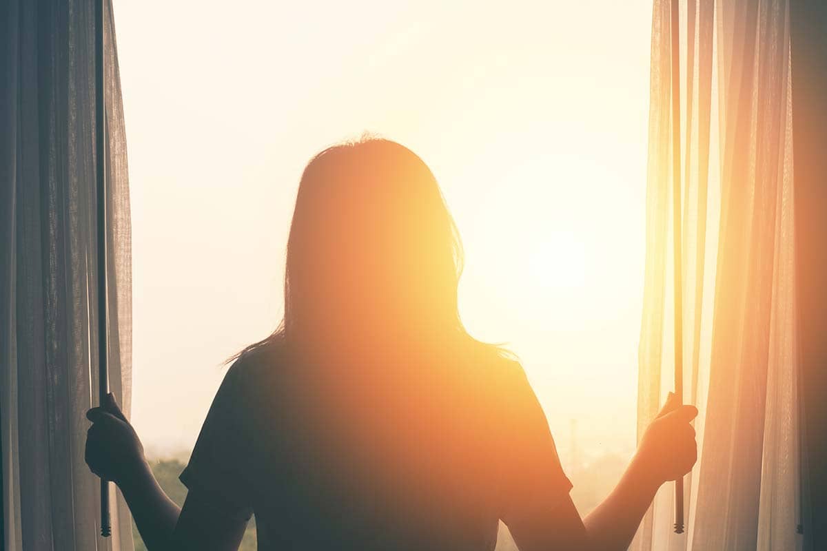 woman opening up curtains to watch sunrise knowing drug and alcohol rehab works