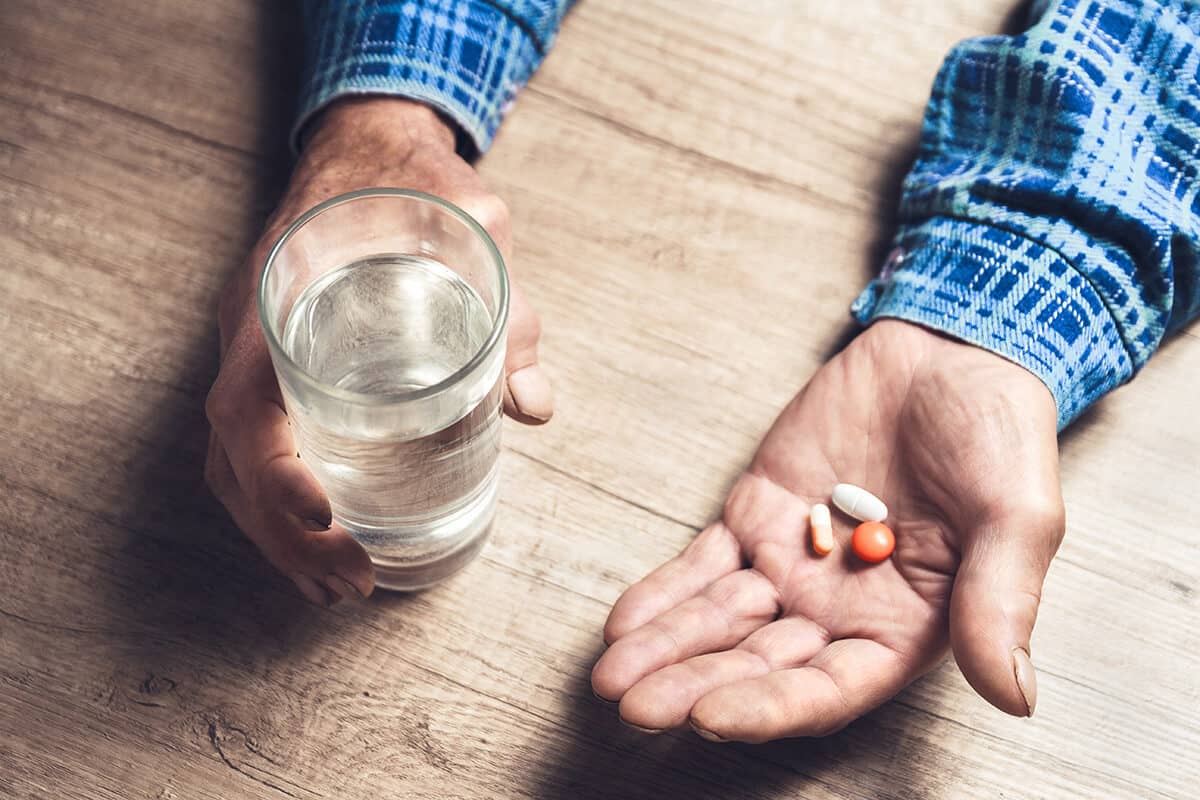 a man holds water and pills and thinks about drug misuse