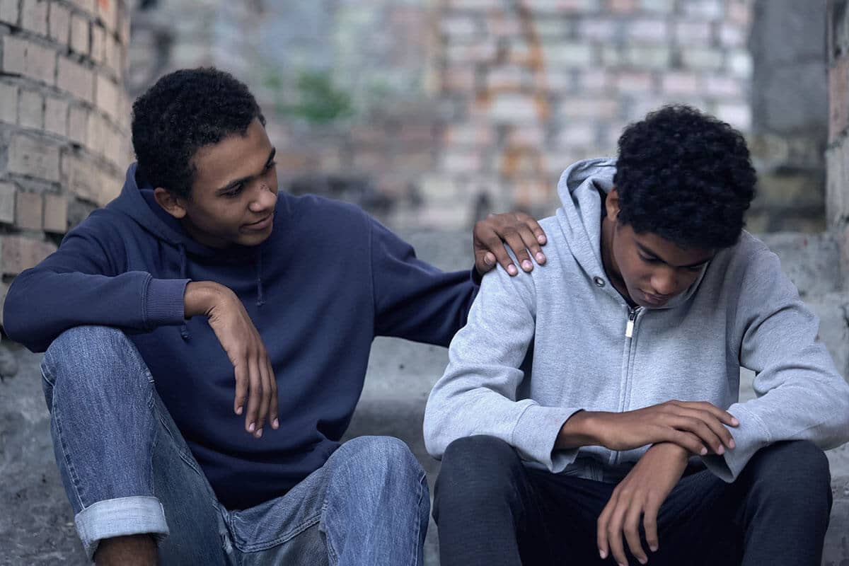 a man puts his hand on his son's shoulder as they discuss alcohol addiction signs in teens