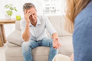 Man on sofa with headache talking to a counselor at one of the centers for substance use treatment.