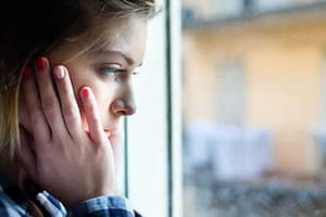 A girl looks out the window with her head in her hands upset about her teen substance use