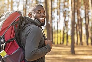 man smiling and backpacking through the woods near drug rehab center near Bellevue, Washington