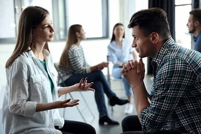 man and woman having a discussion while sitting in group therapy