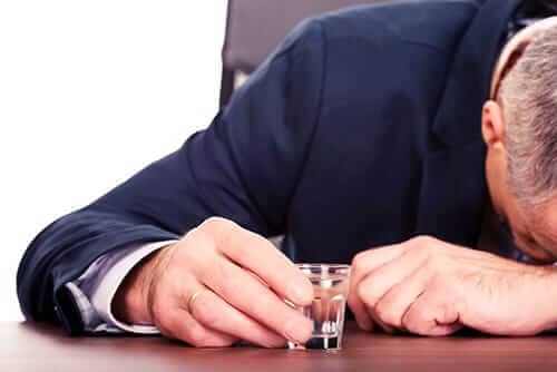 man with shot glass and head on table needs help for alcoholics