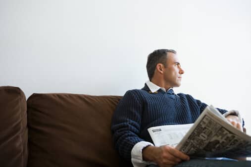 a man sits on a couch at an intensive outpatient program for substance use and reads the newspaper