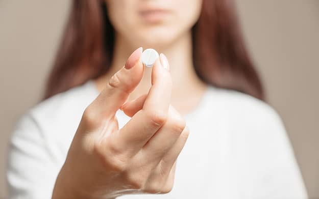 a woman holds a white pill and wonders about the opiate definition