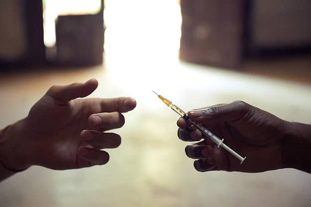 a man handing someone a needle and drugs representing alcohol and drug abuse