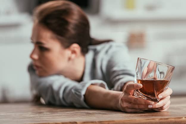 a woman pushes away a glass of alcohol as she thinks about mental health and substance use