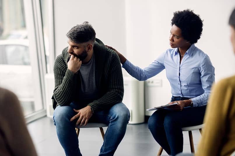 woman with a supportive hand on man's shoulder during group therapy for addiction