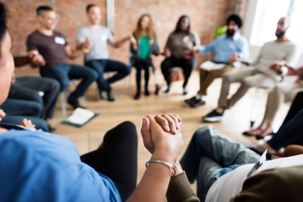 circle of people sitting and holding hands in group therapy for addiction