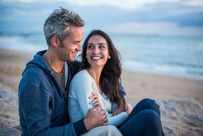 couple sitting on a beach looking at each other and smiling