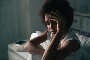 Woman in dark bedroom dealing with opiate withdrawal symptoms.