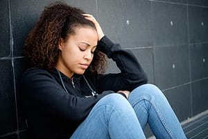 Depressed young woman sitting against wall struggling with symptoms of heroin withdrawal.