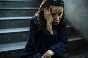 Sad woman on dark steps suffering from one of many mental health disorders.