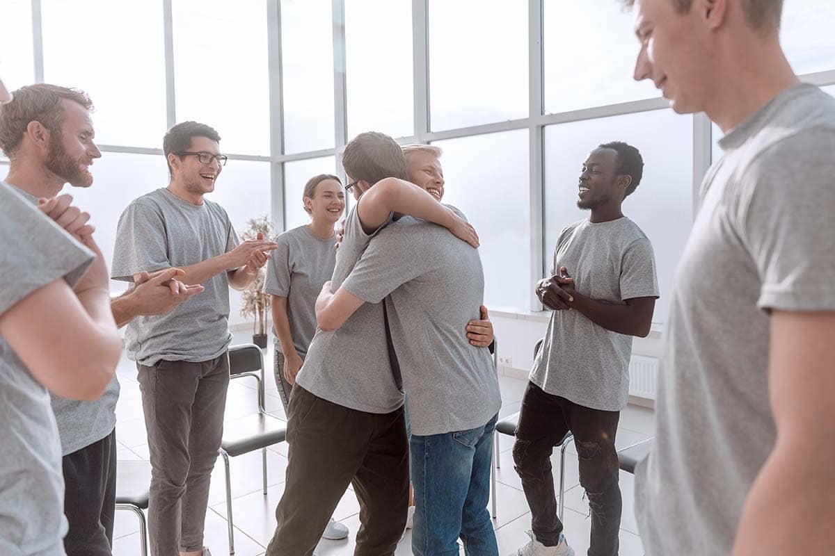 two men hugging during group therapy for addiction treatment to get the benefits of group therapy