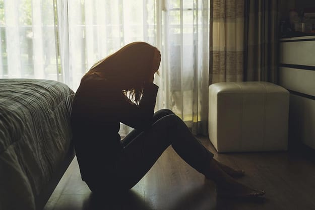 a woman hunched at the foot of her bed suffering from a gateway drug addiction