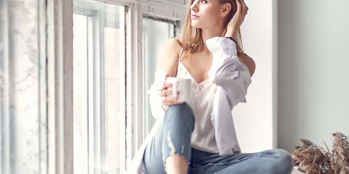 a woman sits by a window and drinks coffee as she thinks about going to detox