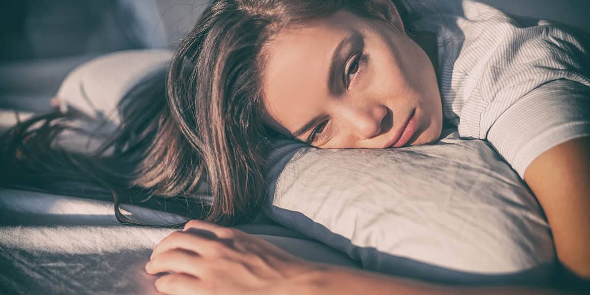 depressed woman in bed hugging pillow displaying one of 5 signs of alcoholism in women