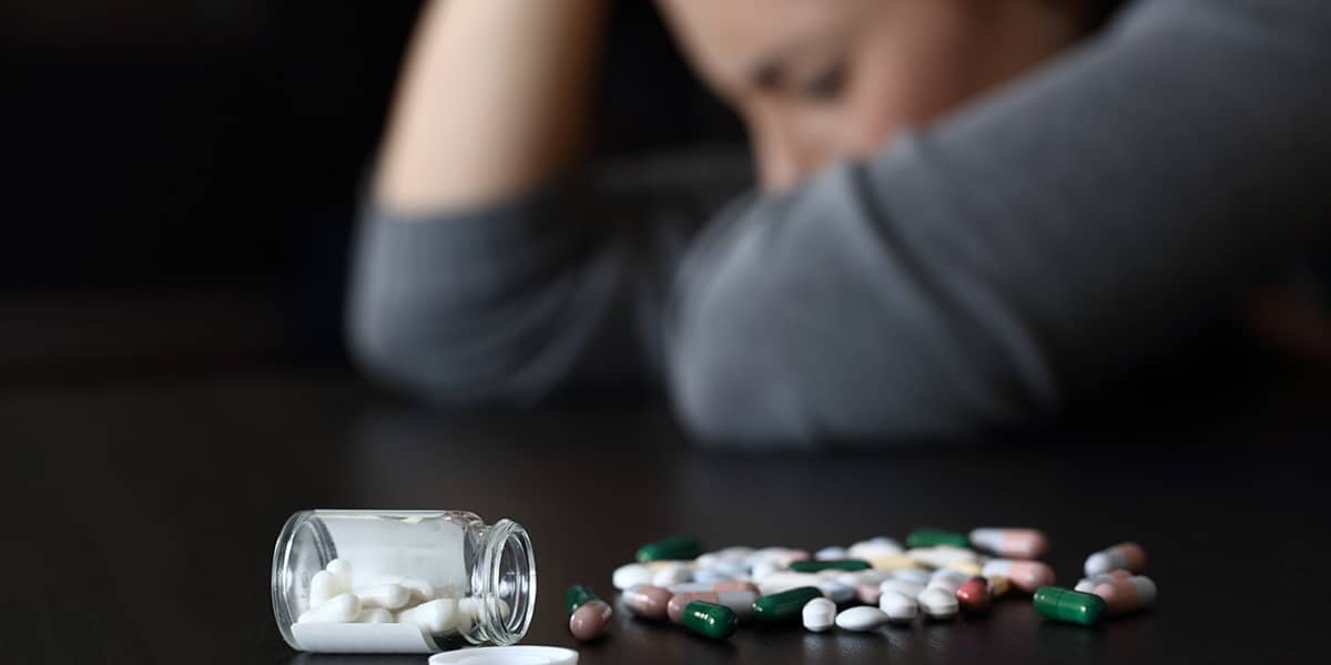 Pills spilled on the table next to a woman struggling with clonazepam abuse