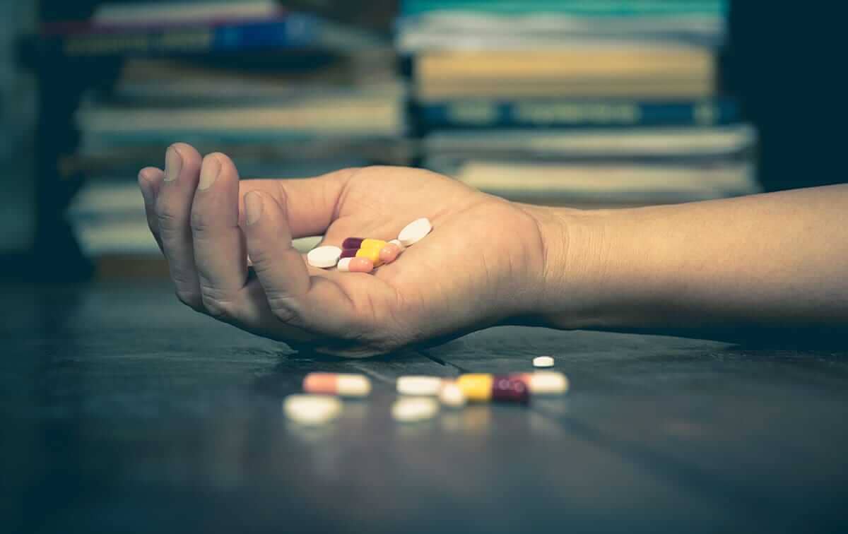 woman holds pills after falling to the ground noticing her drug overdoses symptoms
